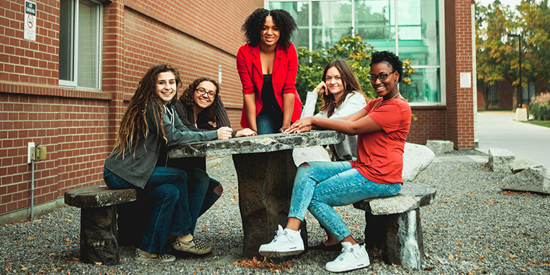 A smiling group of girls sit at a stone table outdoors